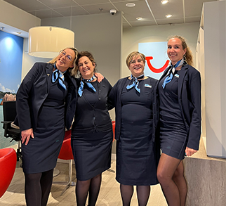 A group of 4 retail colleagues wearing TUI uniform are stood smiling looking at the camera. The two colleagues on the left of the picture are leaning into each other.