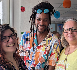 A TUI colleague wearing uniform, a blue TUI shirt with a TUI lanyard. They are smiling at the camera with their laptop in front of them. Behind them is a window on what looks to be a sunny day.