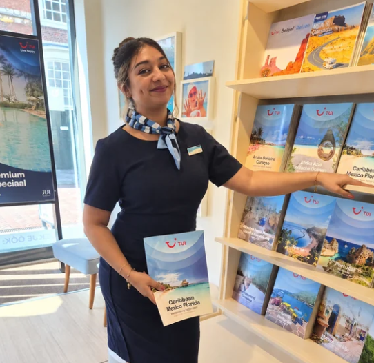 TUI team member holding a Caribbean Mexico & Florida brochure next to a display of TUI holiday brochures in a travel shop.