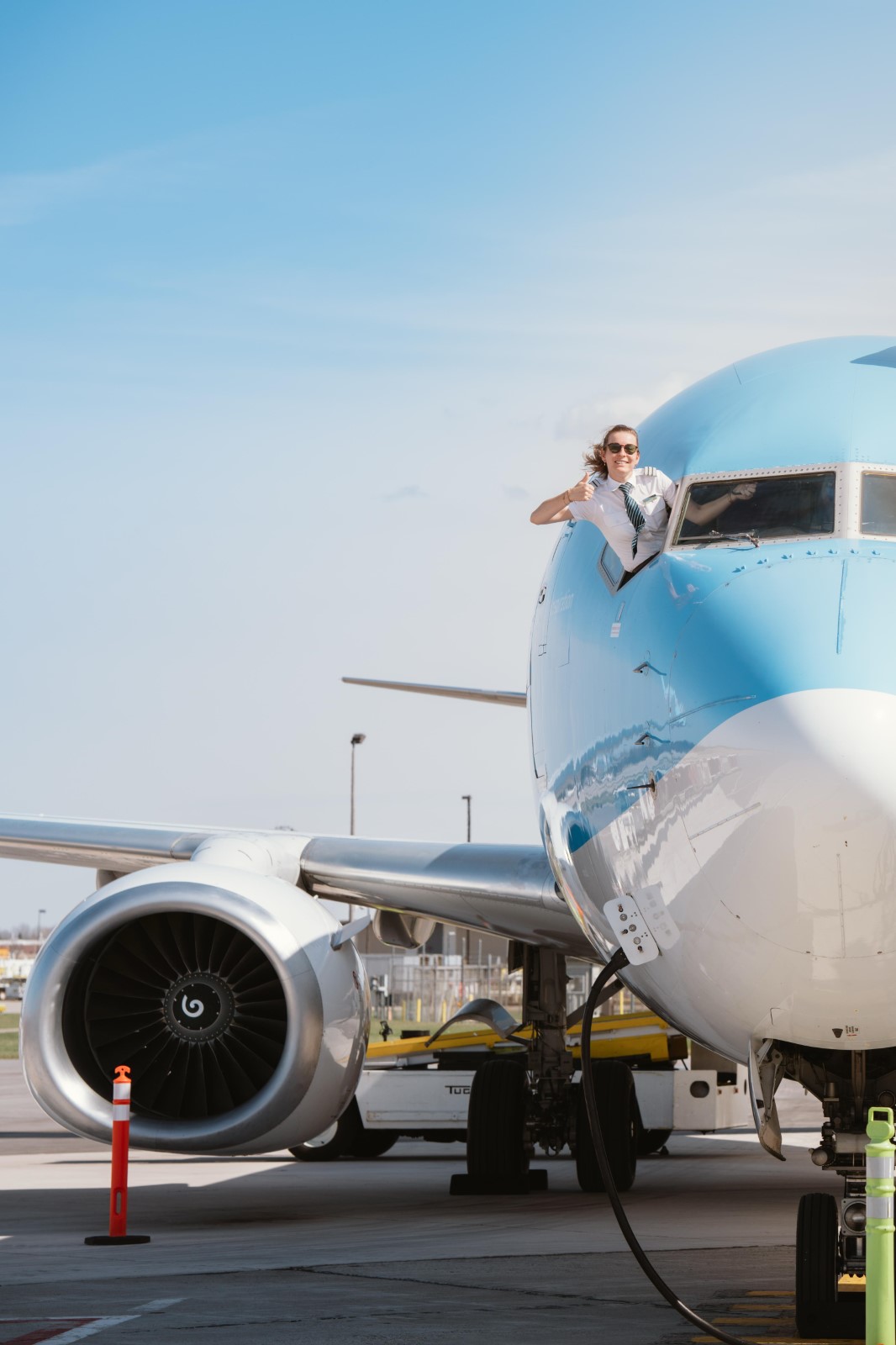 Pilot in uniform giving a thumbs-up while leaning out of an airplane cockpit window