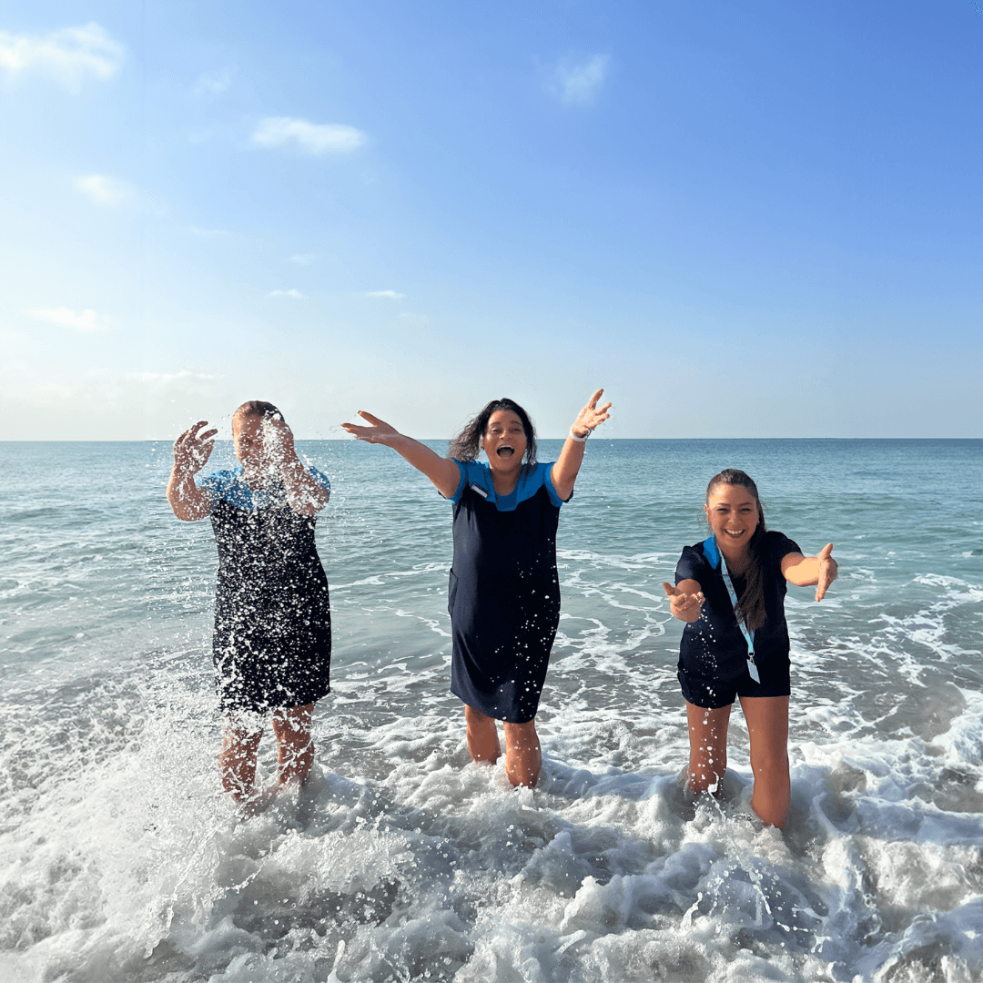 Person in TUI uniform with name tag standing in front of palm trees and a swimming pool.