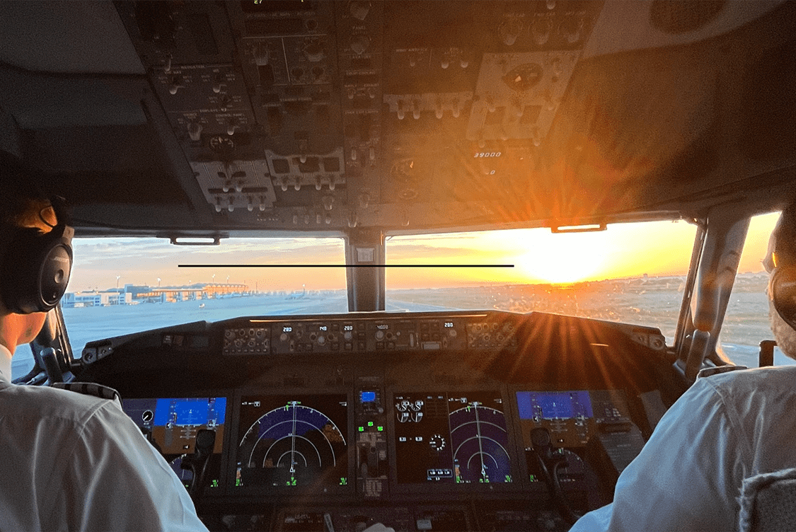 Two pilots in a cockpit preparing for takeoff at sunrise, with flight instruments and controls visible