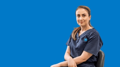 Professional in navy scrubs seated on blue backdrop