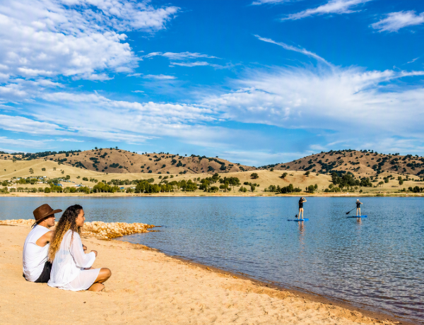 People on sandy shore watching paddleboarders