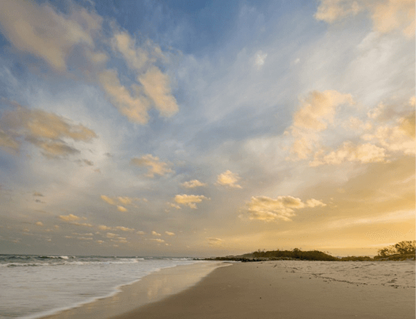 Beach shoreline under cloudy sunset sky