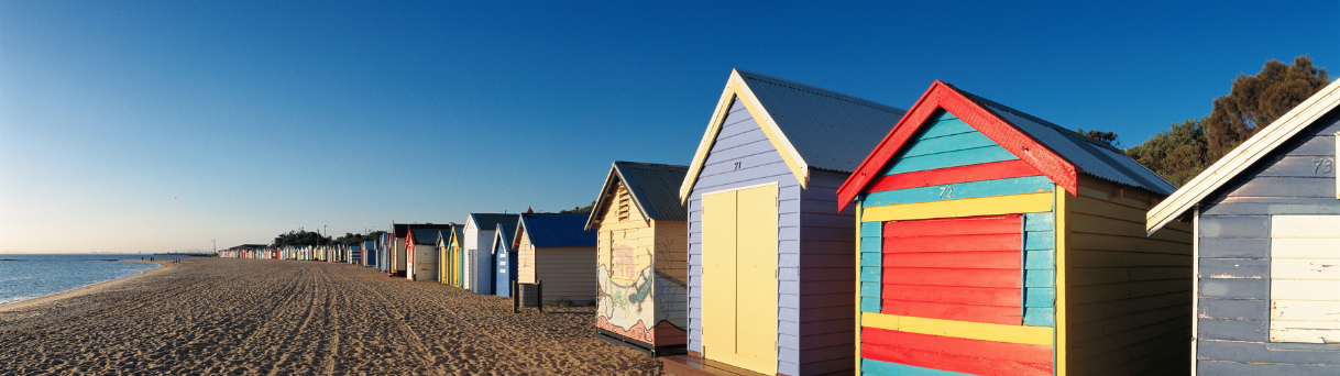 Colorful beach huts line sandy shore under blue sky