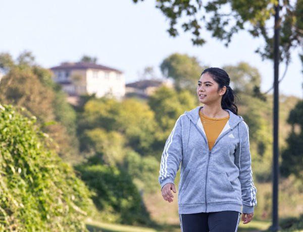 Person walking outdoors on a leafy park pathway.