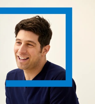 Two people talking in a clinical consultation room, viewed through a blue framed partition.