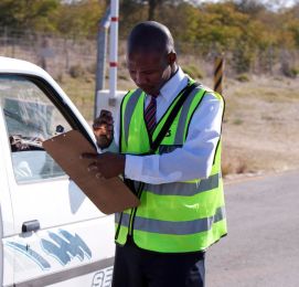 Guard in vest writes on clipboard by car.