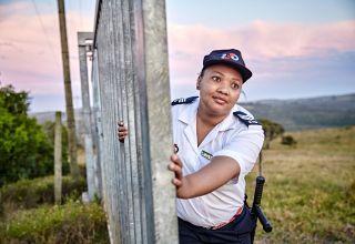 Smiling woman in uniform opens gate outdoors.
