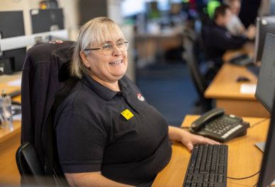 Smiling woman sitting at desk with computer and phone.