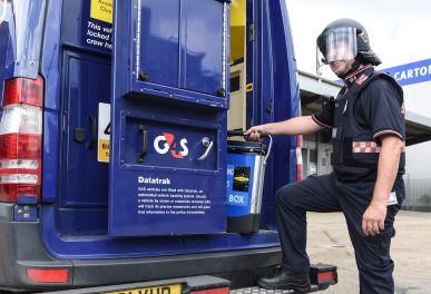 Guard in helmet loads cash box into G4S van.