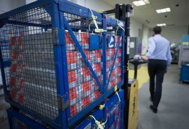 Crate with sealed boxes in warehouse, man walks away.