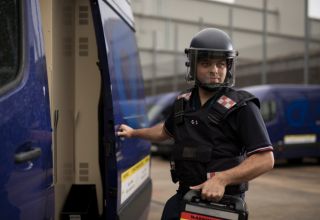 Security guard with helmet opening armoured van door.