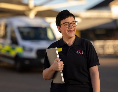 Smiling G4S staff member holding a laptop outside.
