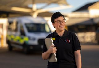 Smiling G4S staff member holding a laptop outside.