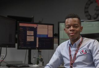 Man at desk with multiple monitors in control room.