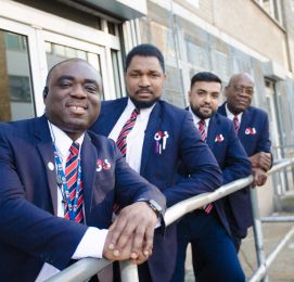 Four G4S employees in uniform standing by railing outside.