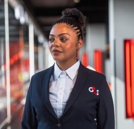 Woman in a blue shirt and red tie standing by a wall.