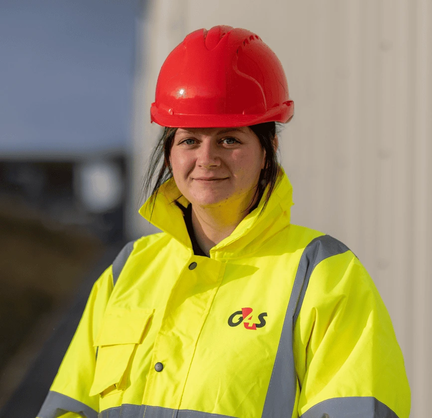 Portrait of a worker wearing a red hard hat and a yellow high-visibility jacket with the G4S logo.