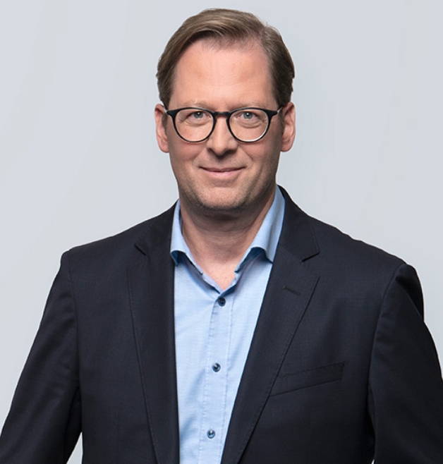 Man in suit with glasses before a plain grey bgpic