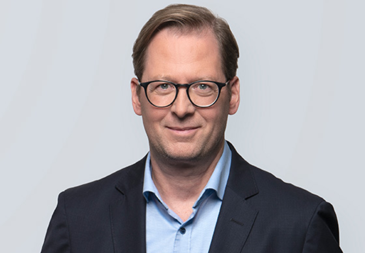 Mann mit Brille im dunklen Anzug vor hellem Hintergrund