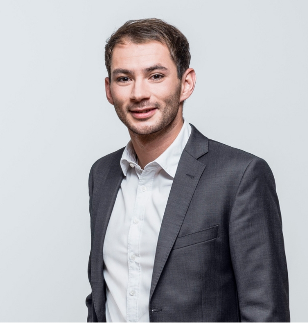 Smiling man in grey suit posing against light backdrop