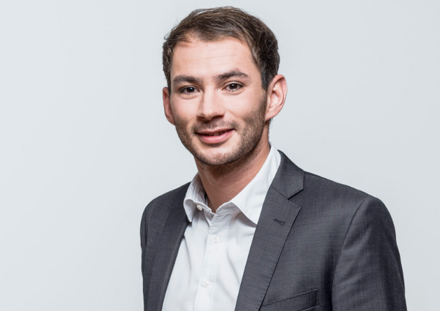 Smiling man in grey suit posing against light backdrop