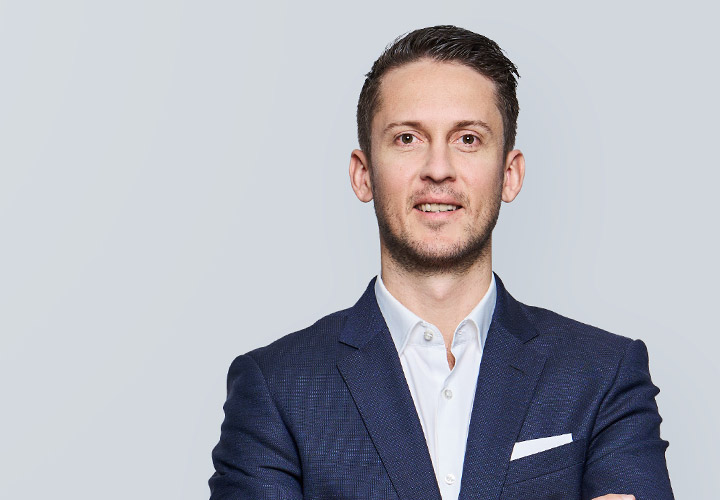 Smiling man in navy suit with arms crossed.