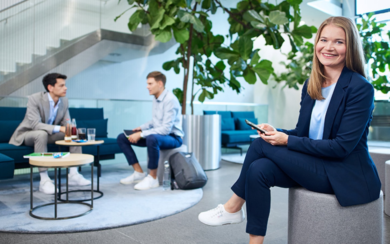 Lächelnde Frau in moderner Lounge, Kollegen im Gespräch