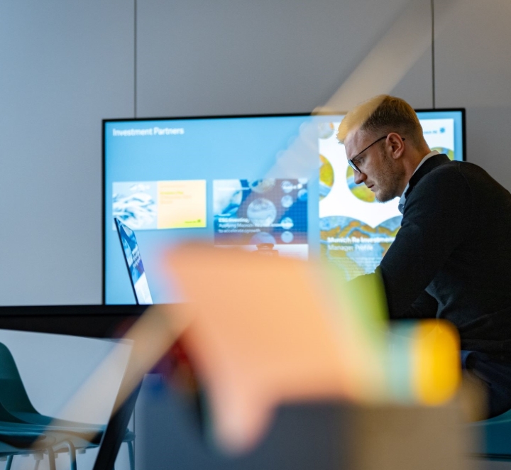 Man in office with screen showing slides.
