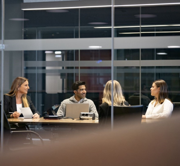 Four people in office meeting with laptop.