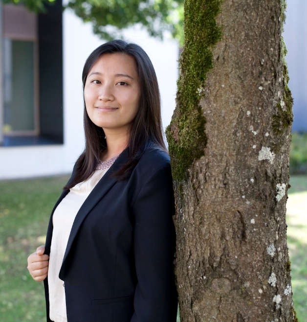 Woman in black blazer stands near a tree.