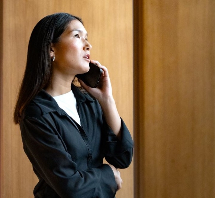 Woman in black jacket talks on phone inside.