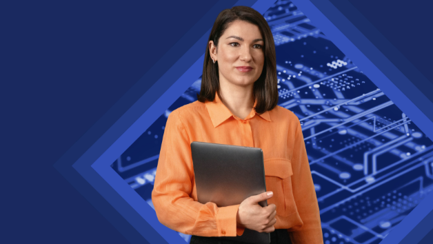 Woman in an orange blouse holding a laptop, standing in front of a technical background.