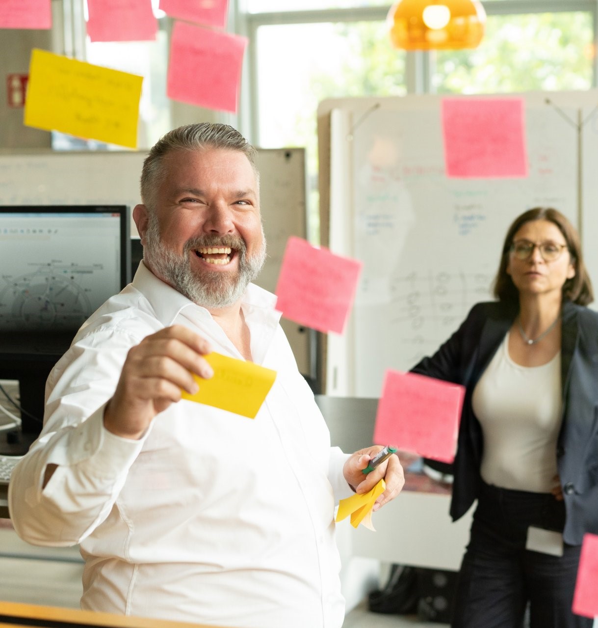 Man working with sticky notes on a screen, woman in the background.