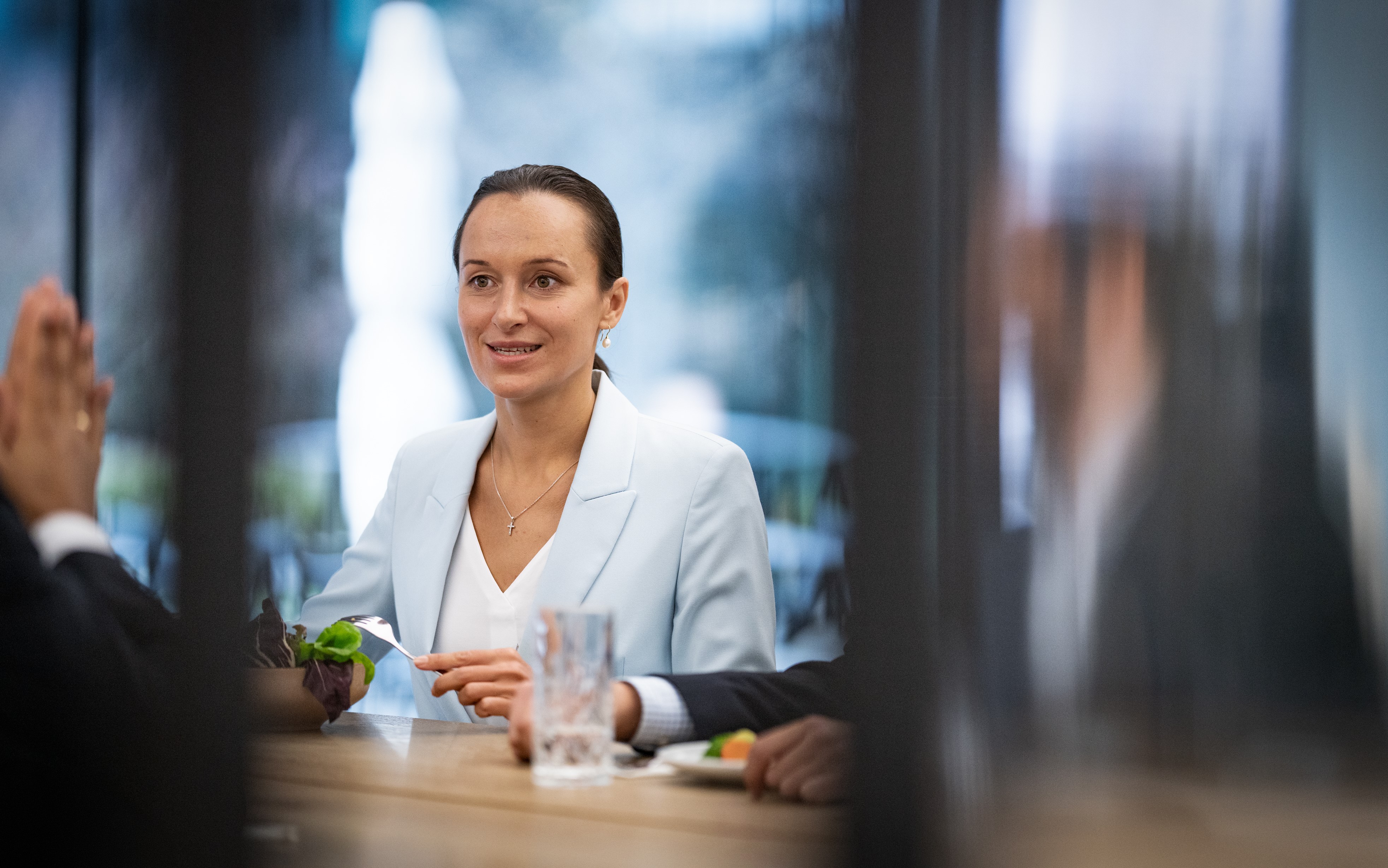 Woman in a white blazer talks to colleagues.
