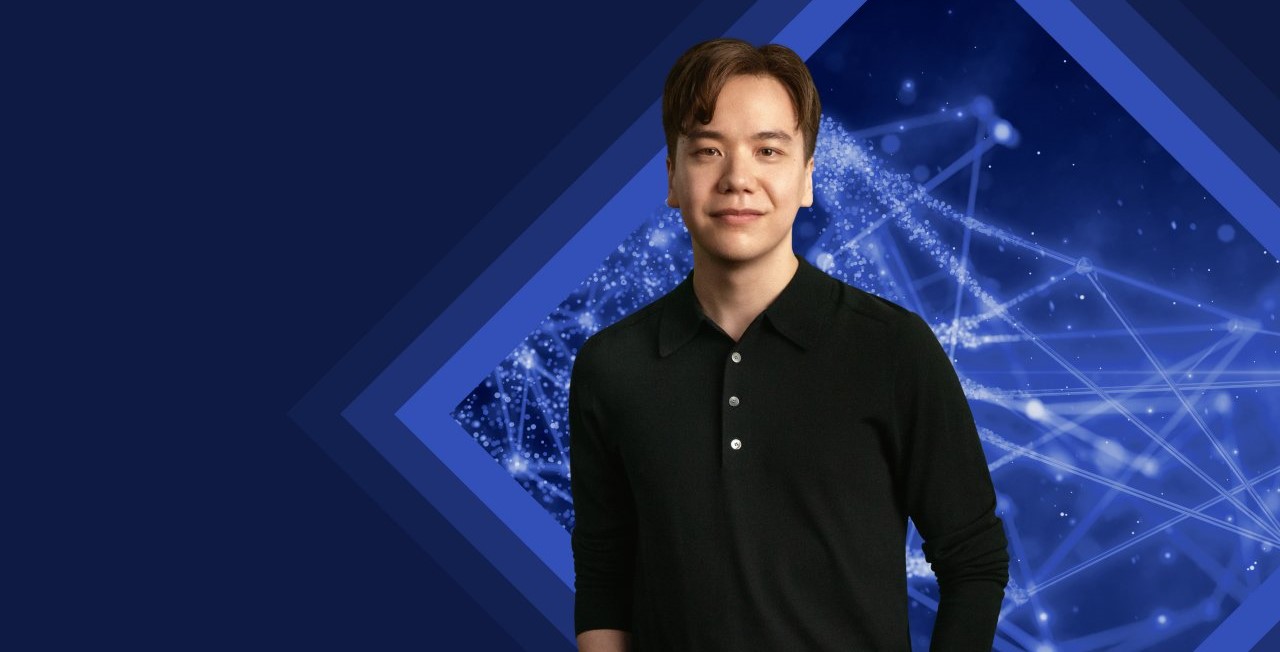 Young man smiling into the camera, standing in front of a technical background