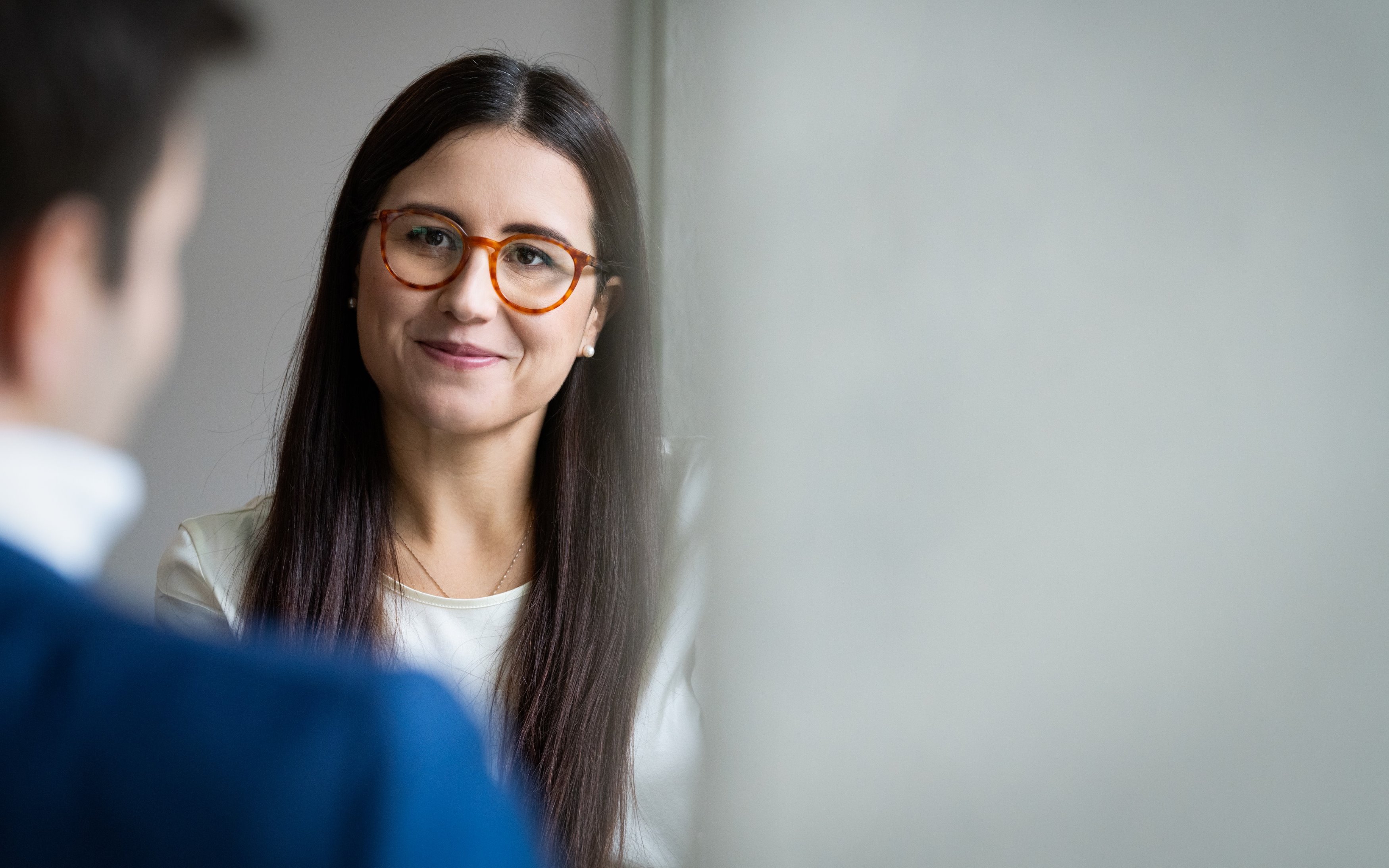Woman with long brown hair talking to a colleage.