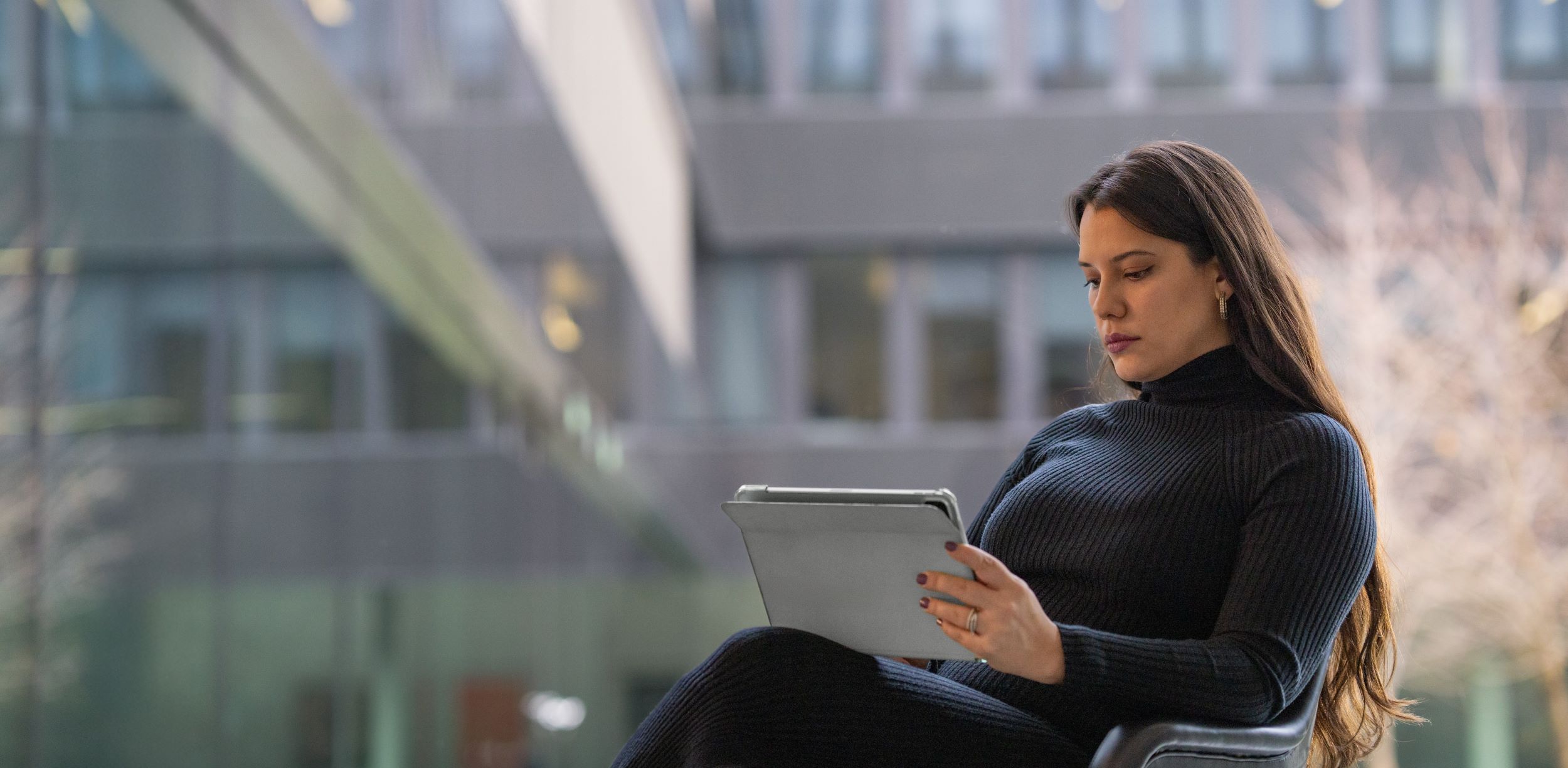 Young woman working at a laptop, sitting in a modern office environment.