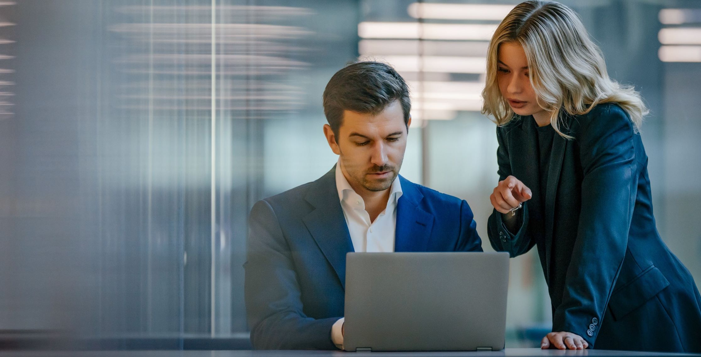 Two colleagues working on a laptop in a business environment.