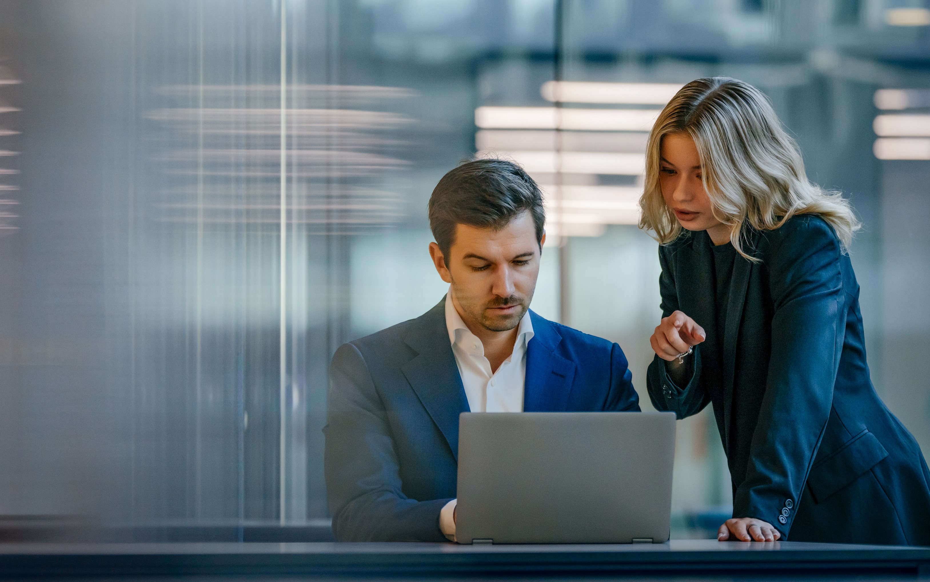 Two colleagues working on a laptop in a business environment.