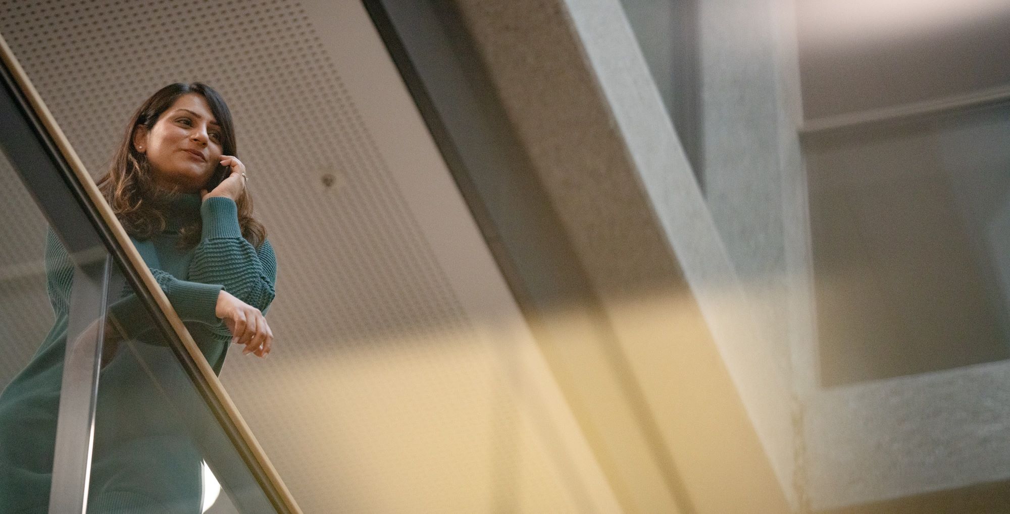Young woman leaning at a gallery in an office indoor atrium.