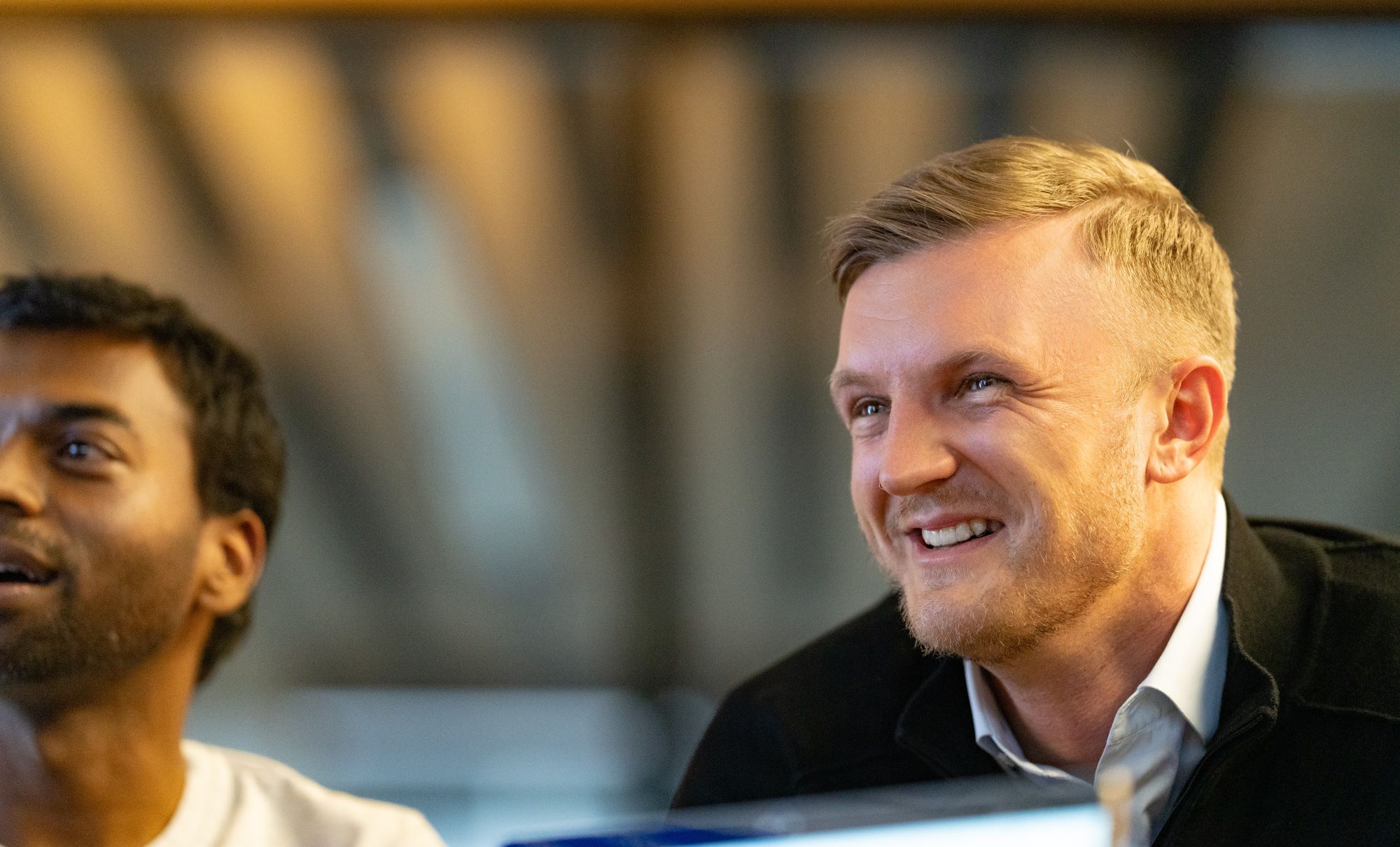 Young man smiling to another  person, second person in the background