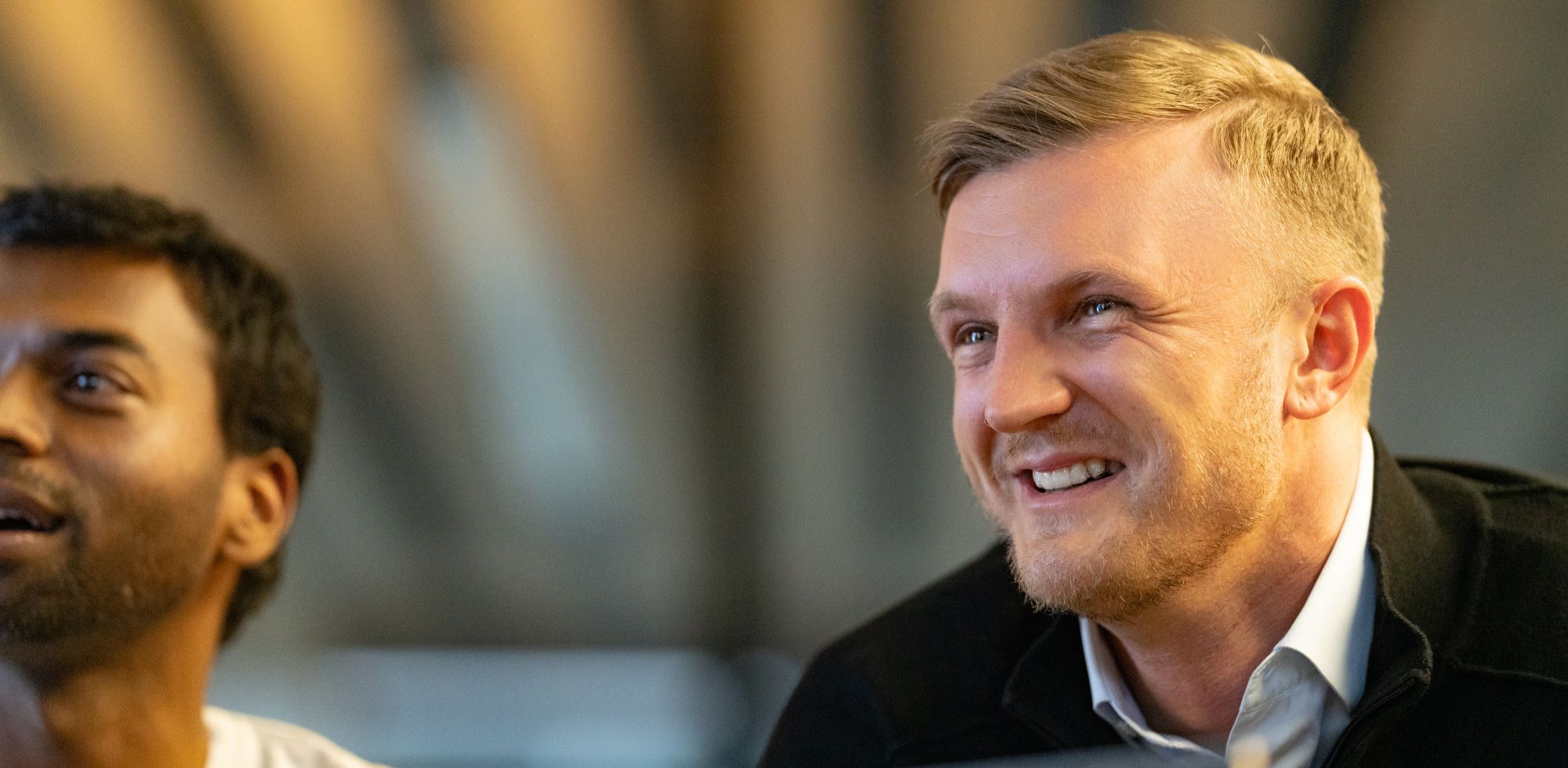 Face of a young man smiling, second man in the background.