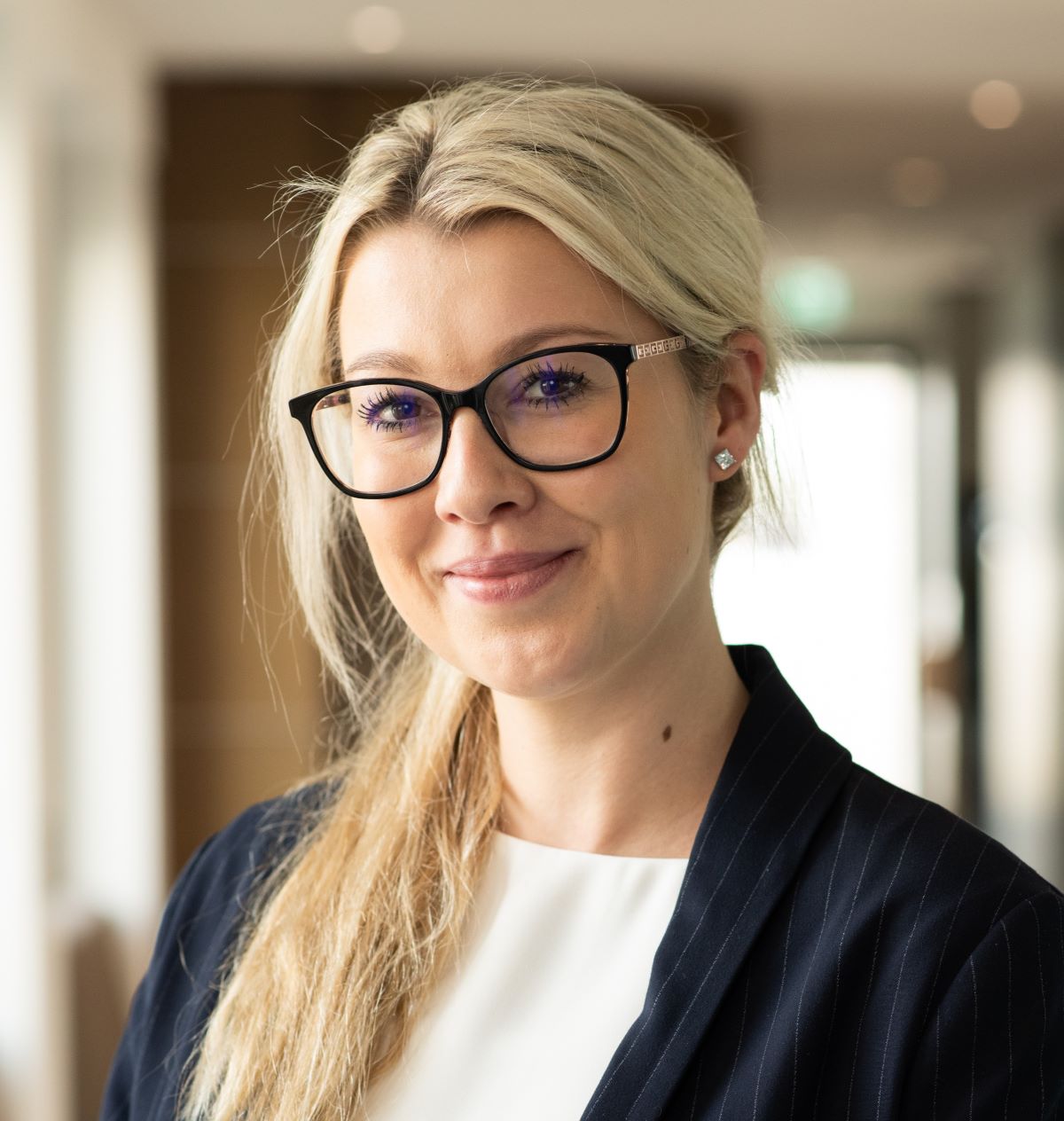 Frau im Business Outfit lächelt in die Kamera.