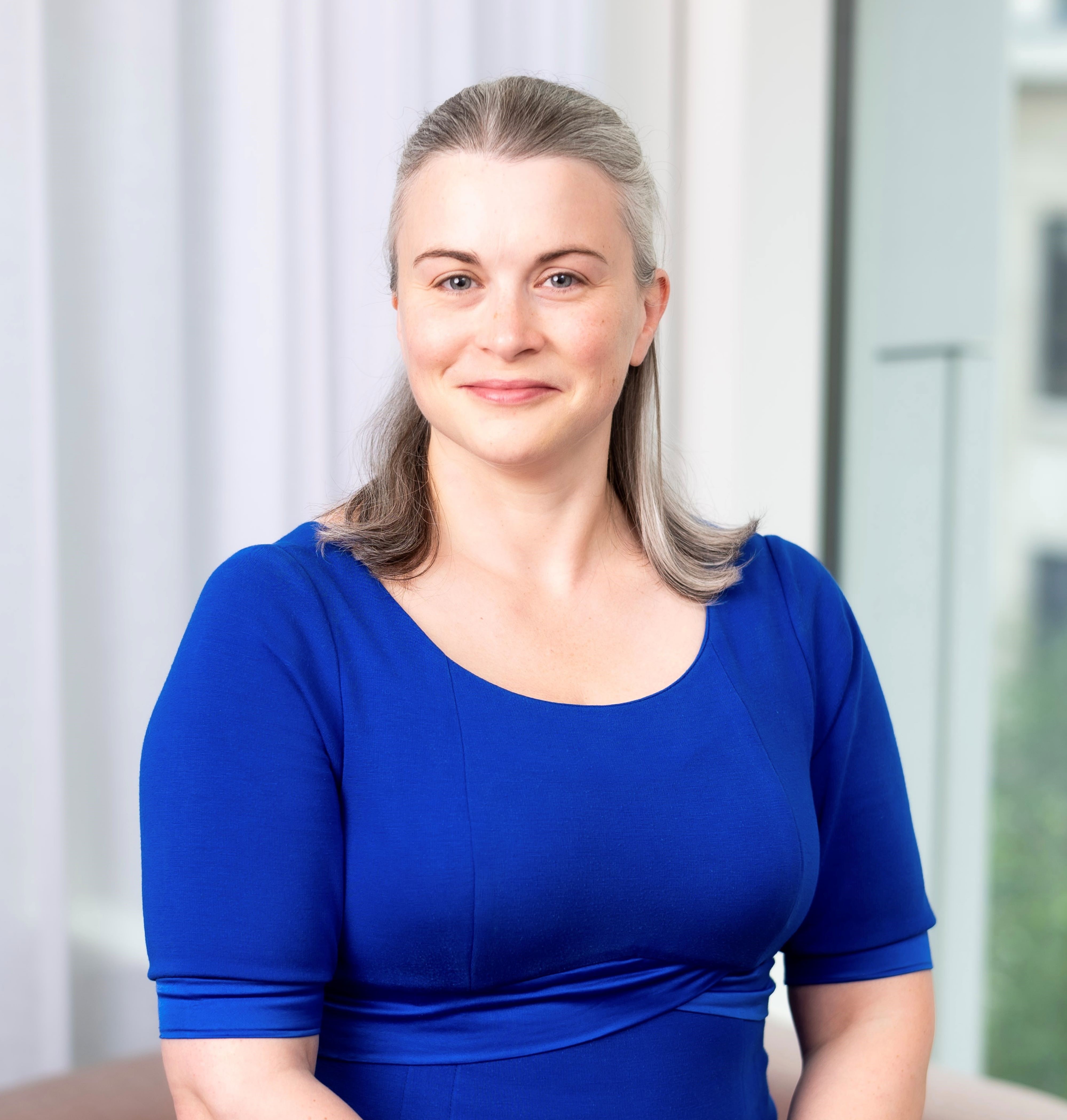 Smiling woman in a blue dress with grey hair and blue eyes