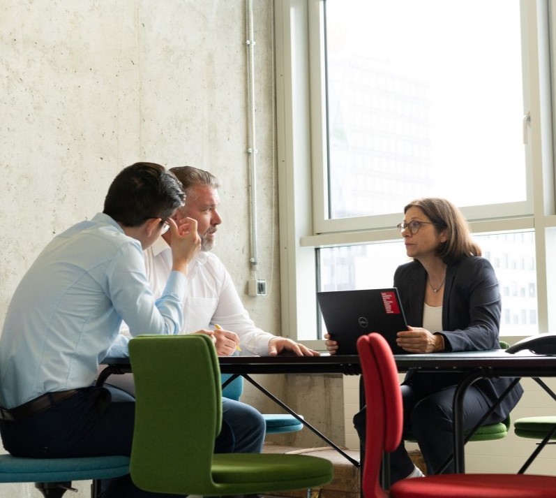 Group of three employees at a table discussing business topics.