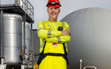 Man in geel pak met helm bij industriële tanks