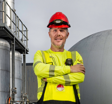 Man in geel pak met helm bij industriële tanks